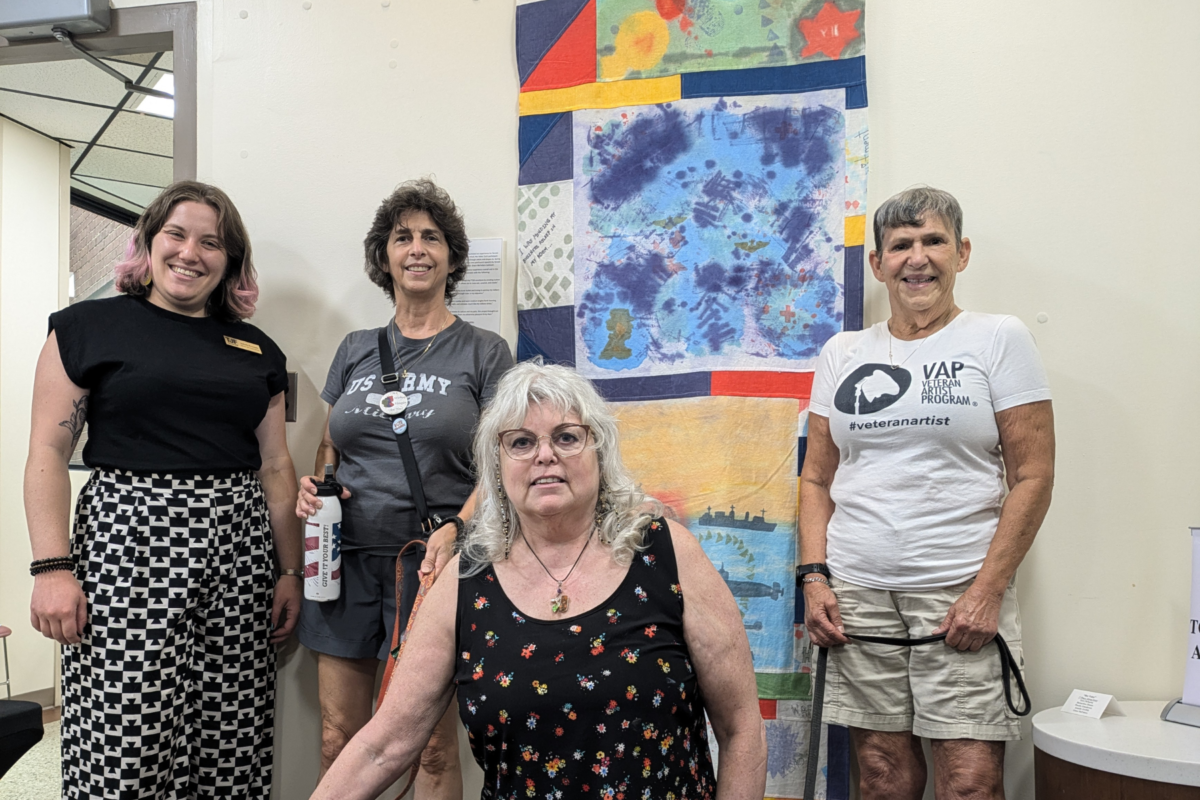 First Place - TJF 'Her Valor' Fiber Arts Group Project. Picture of women who participated in the Her Valor Fiber Arts Project standing next to their final project, which received first place in the competition.