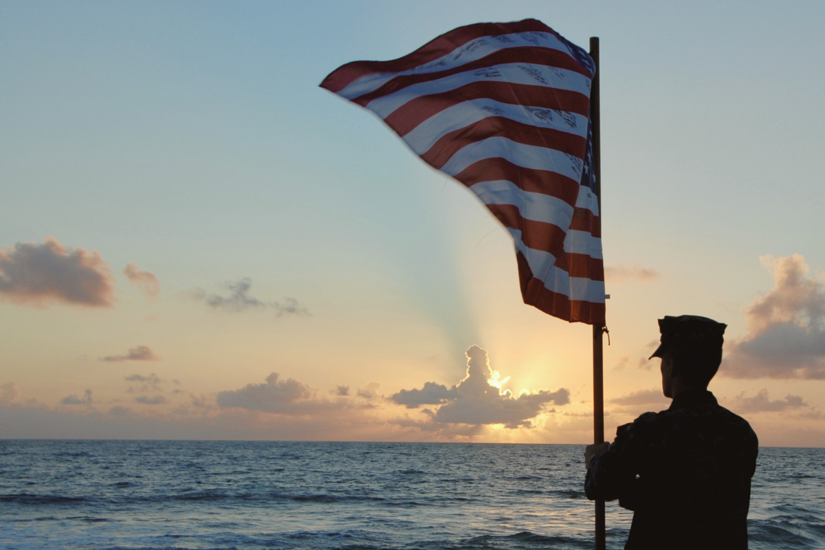 Soldier holding the American flag at a sunset on the beach. The Joel Fund - Reconnecting Veterans to Life at Home - Building connection, restoring purpose, creating stability